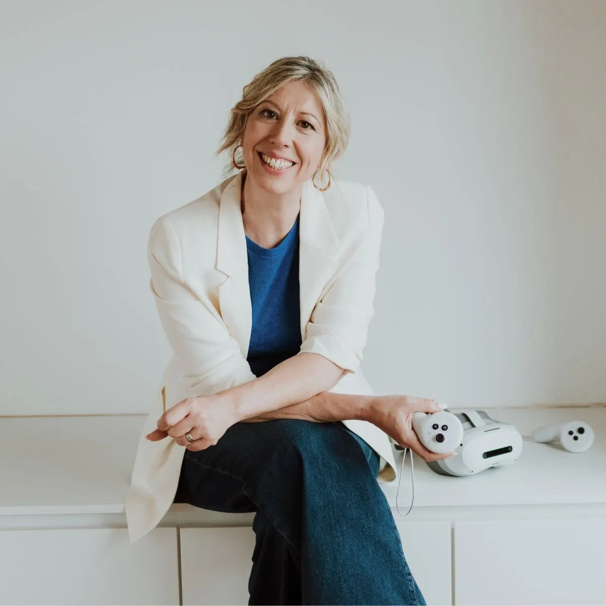 Elke Van Parys lacht in de camera met een VR-bril en controller naast zich op een wit meubel